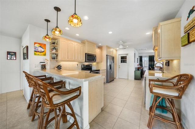 kitchen featuring kitchen peninsula, a breakfast bar, stainless steel appliances, light brown cabinets, and pendant lighting