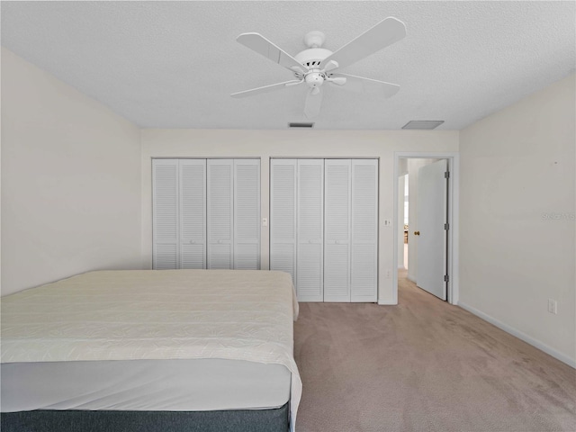 unfurnished bedroom featuring multiple closets, ceiling fan, light carpet, and a textured ceiling