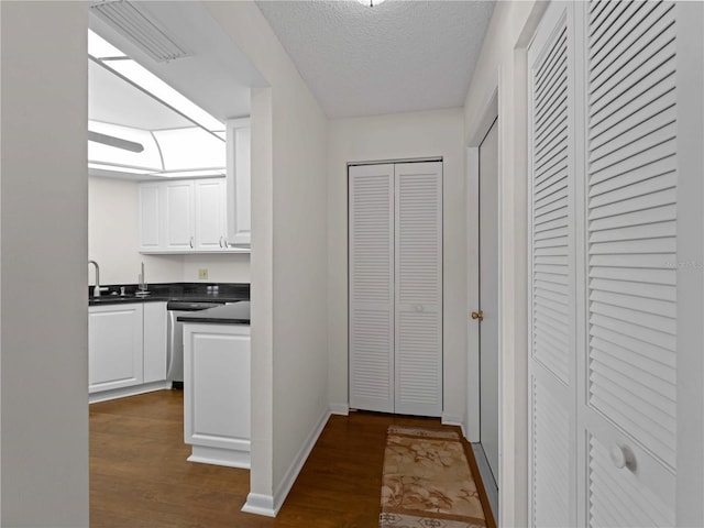 kitchen with sink, dark hardwood / wood-style flooring, stainless steel dishwasher, a textured ceiling, and white cabinets