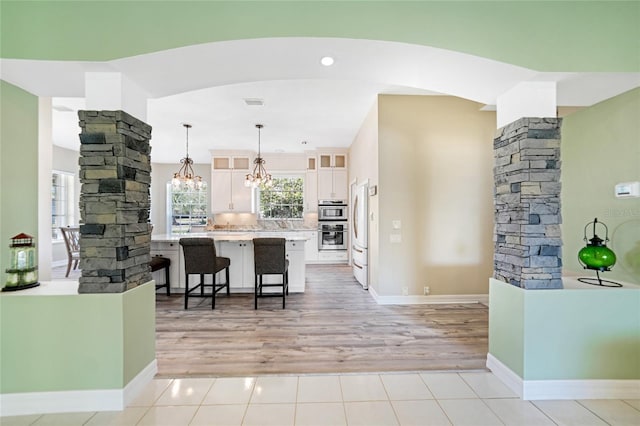 kitchen with a kitchen breakfast bar, decorative columns, pendant lighting, light hardwood / wood-style floors, and white cabinetry