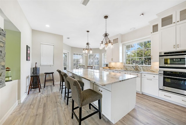 kitchen featuring white cabinetry, light hardwood / wood-style flooring, a kitchen island, and pendant lighting