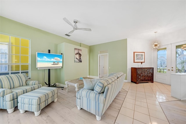 living room featuring light tile patterned floors, ceiling fan with notable chandelier, and french doors