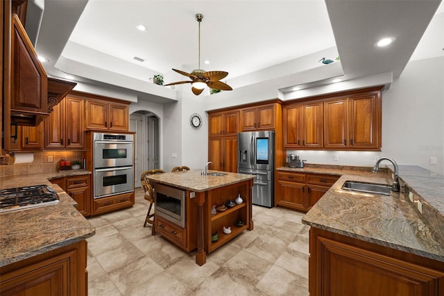 kitchen with a center island with sink, sink, ceiling fan, light stone countertops, and appliances with stainless steel finishes