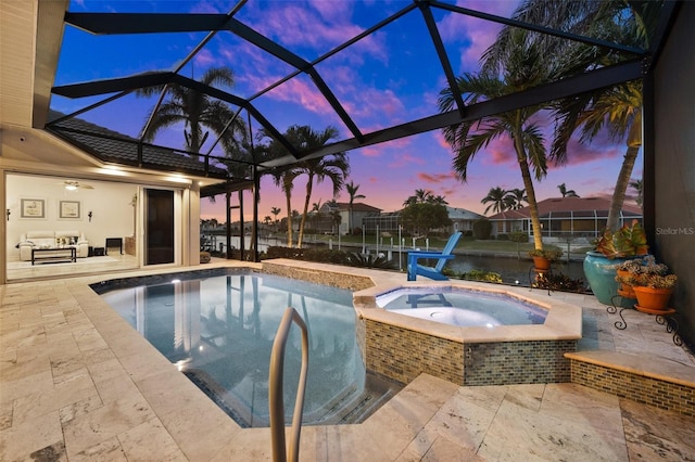 pool at dusk featuring a lanai, a patio area, and an in ground hot tub