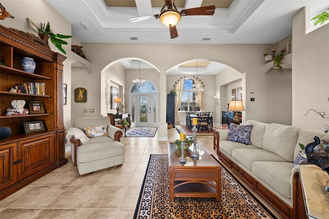 living room with a tray ceiling, light tile patterned floors, ceiling fan with notable chandelier, and ornamental molding