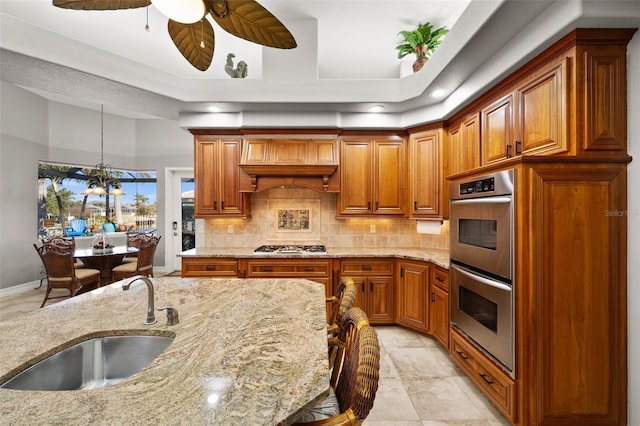 kitchen with pendant lighting, sink, decorative backsplash, light stone countertops, and stainless steel appliances