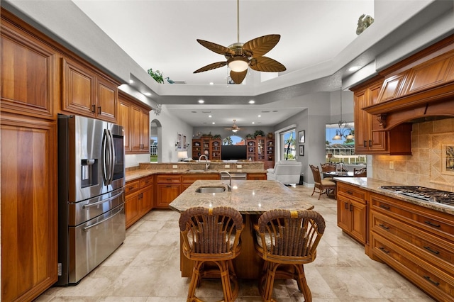 kitchen featuring a kitchen bar, a center island with sink, light stone counters, kitchen peninsula, and stainless steel appliances