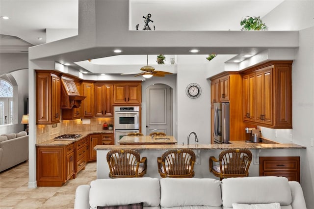 kitchen with ceiling fan, stainless steel appliances, light stone counters, kitchen peninsula, and a kitchen bar