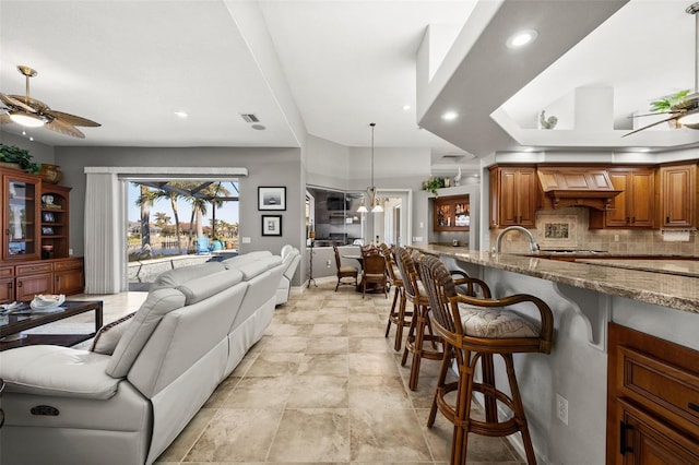 interior space with light stone countertops, custom exhaust hood, ceiling fan, pendant lighting, and a breakfast bar area