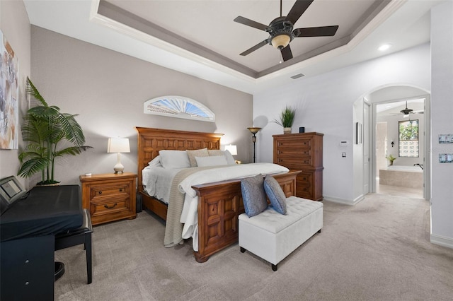 carpeted bedroom with a raised ceiling, ensuite bath, and ceiling fan