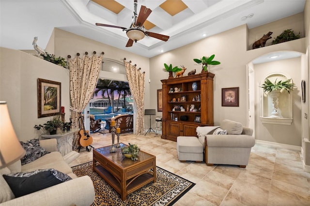 living room featuring ceiling fan, coffered ceiling, beamed ceiling, a towering ceiling, and ornamental molding