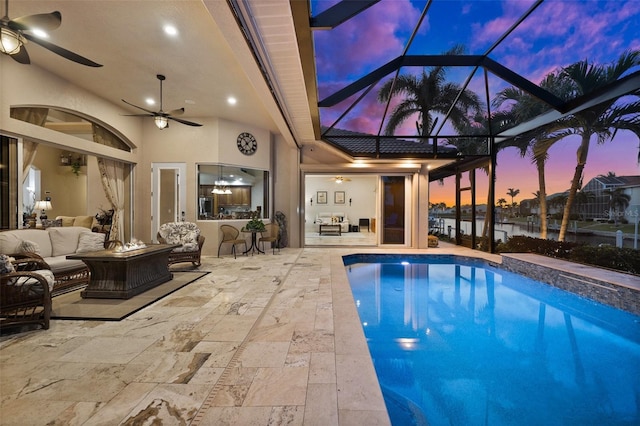 pool at dusk featuring a patio, an outdoor hangout area, glass enclosure, and ceiling fan