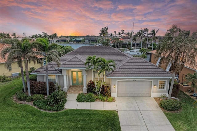 view of front of house featuring a lawn, french doors, a water view, and a garage