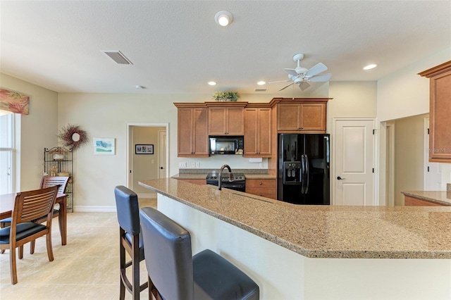 kitchen with light stone countertops, ceiling fan, a textured ceiling, a breakfast bar, and black appliances