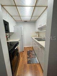 kitchen featuring a paneled ceiling, white cabinetry, black appliances, and light wood-type flooring