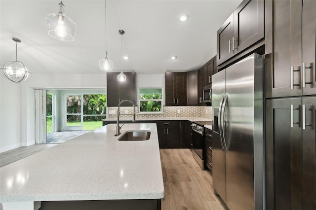 kitchen with light hardwood / wood-style flooring, stainless steel appliances, hanging light fixtures, and an island with sink