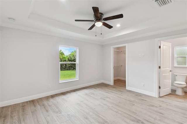 unfurnished bedroom with ceiling fan, a walk in closet, a tray ceiling, and ensuite bath