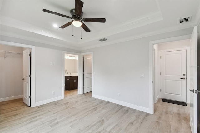 unfurnished bedroom featuring ceiling fan, light hardwood / wood-style floors, a tray ceiling, a walk in closet, and a closet