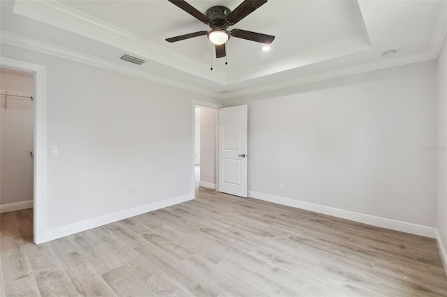 unfurnished bedroom with ornamental molding, a raised ceiling, ceiling fan, a spacious closet, and a closet