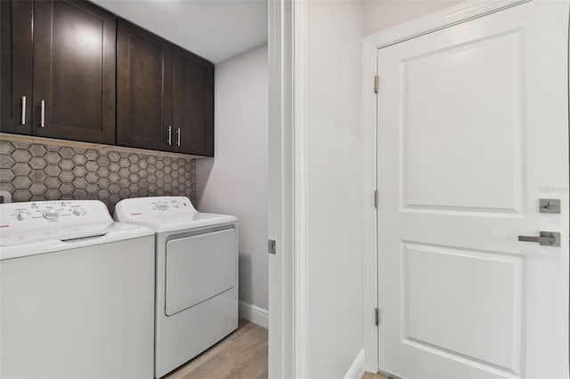 clothes washing area with washing machine and dryer, light hardwood / wood-style flooring, and cabinets