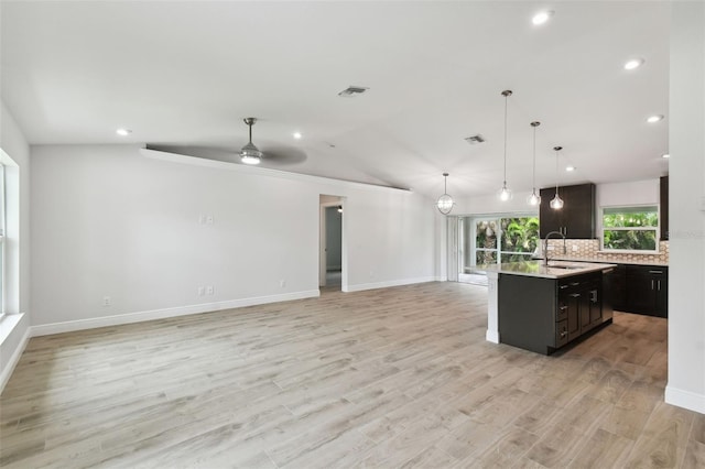 kitchen with ceiling fan, hanging light fixtures, light hardwood / wood-style flooring, vaulted ceiling, and a center island with sink