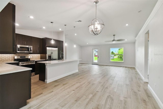 kitchen with pendant lighting, vaulted ceiling, a kitchen island with sink, appliances with stainless steel finishes, and light wood-type flooring