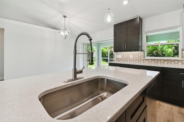 kitchen with light stone countertops, decorative backsplash, dark brown cabinetry, crown molding, and sink