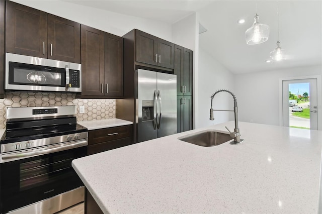 kitchen with light stone counters, sink, stainless steel appliances, and decorative light fixtures