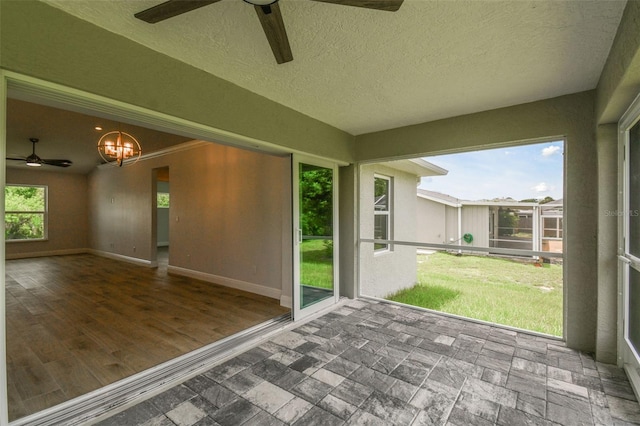 unfurnished sunroom with ceiling fan with notable chandelier