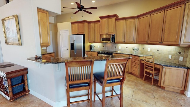 kitchen with decorative backsplash, kitchen peninsula, dark stone counters, stainless steel appliances, and a breakfast bar area