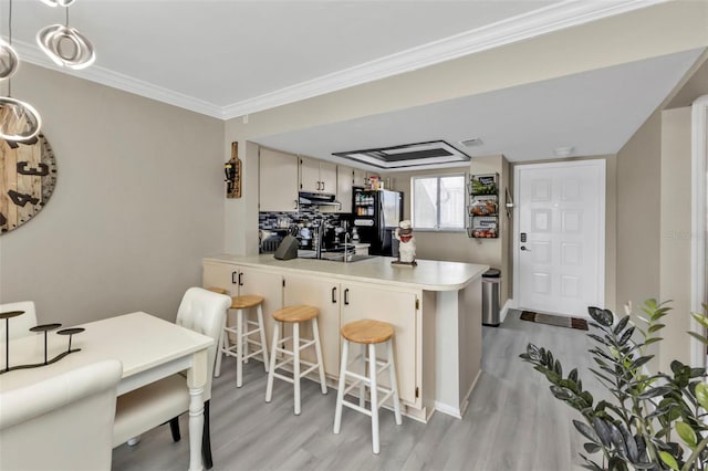 kitchen with a breakfast bar, black fridge, ornamental molding, kitchen peninsula, and light hardwood / wood-style floors