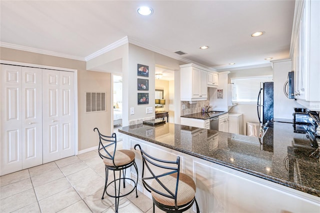 kitchen with kitchen peninsula, a kitchen breakfast bar, white cabinetry, and dark stone countertops