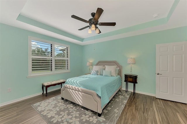 bedroom featuring ceiling fan, dark hardwood / wood-style floors, and a raised ceiling