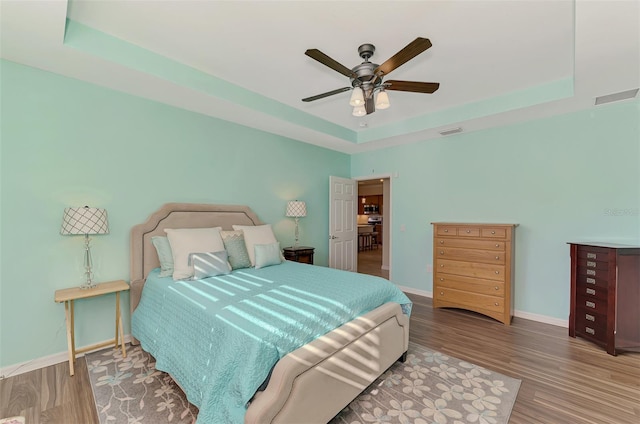 bedroom with hardwood / wood-style flooring, ceiling fan, and a raised ceiling