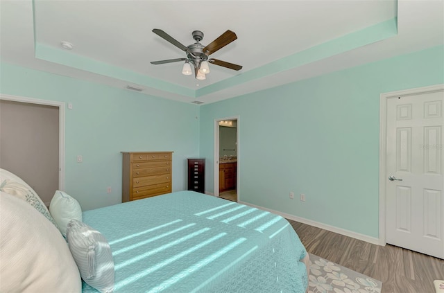 bedroom featuring a tray ceiling, ceiling fan, light hardwood / wood-style floors, and ensuite bathroom