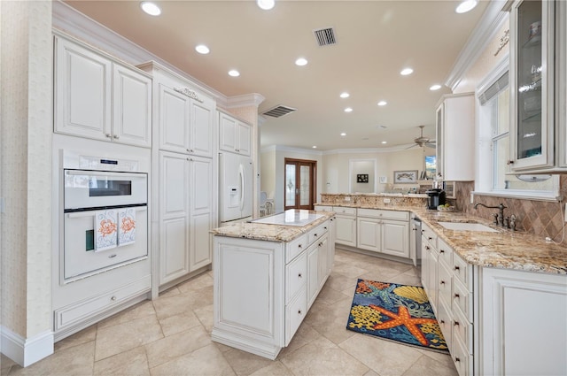 kitchen with a kitchen island, white cabinetry, ornamental molding, kitchen peninsula, and white appliances