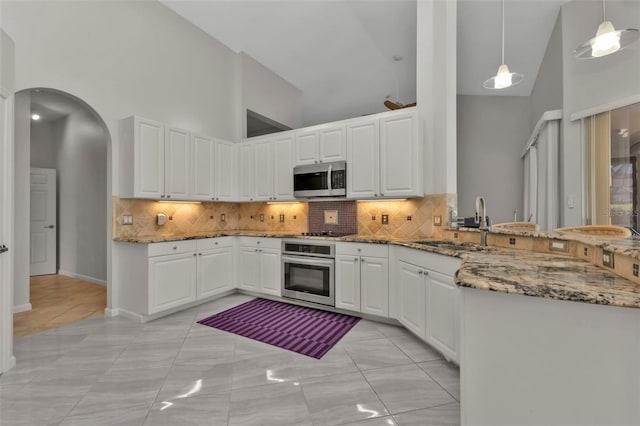 kitchen with appliances with stainless steel finishes, dark stone counters, high vaulted ceiling, white cabinetry, and hanging light fixtures