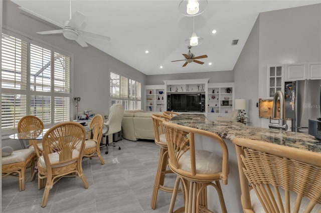 kitchen with a healthy amount of sunlight, stainless steel fridge, white cabinetry, and light stone countertops