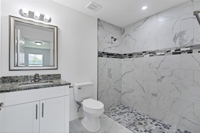 bathroom featuring a tile shower, vanity, and toilet