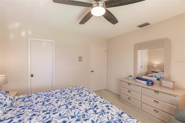 bedroom with ceiling fan, light colored carpet, and a textured ceiling