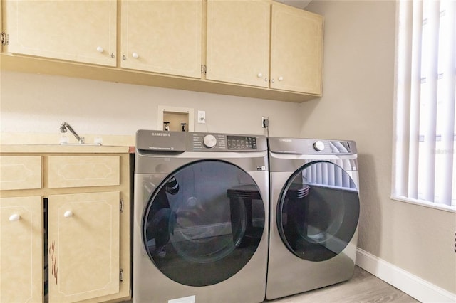 laundry room featuring washing machine and clothes dryer, cabinets, and light wood-type flooring