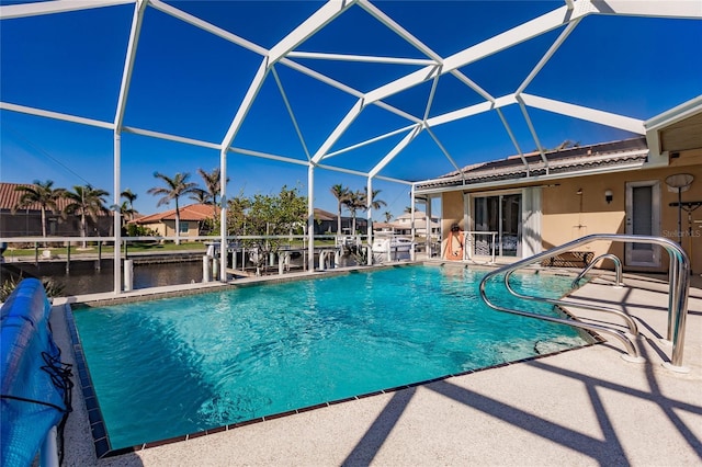 view of pool featuring glass enclosure, a patio area, and a water view