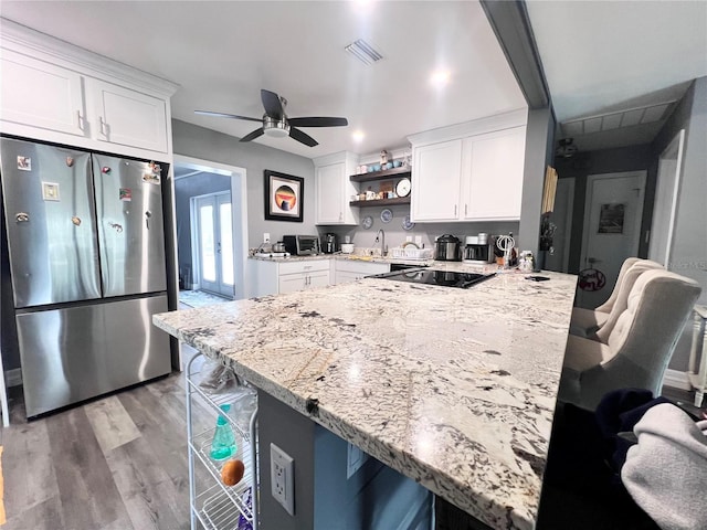 kitchen featuring light stone counters, kitchen peninsula, stainless steel fridge, a breakfast bar, and white cabinets