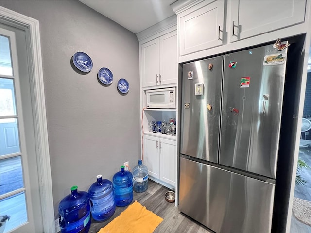 kitchen featuring white microwave, stainless steel fridge, white cabinets, and light hardwood / wood-style floors