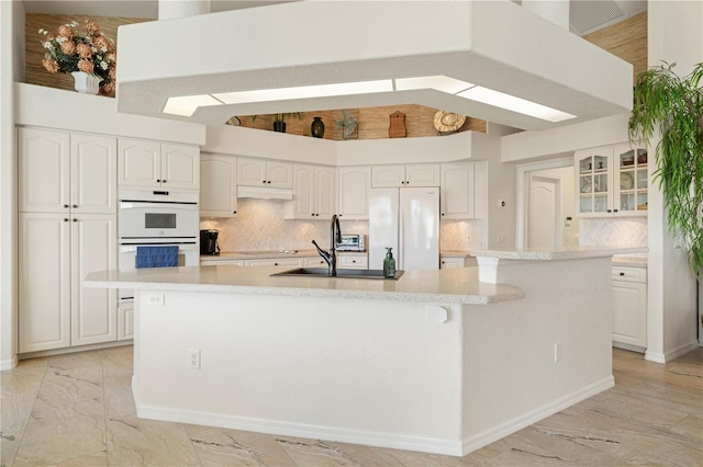 kitchen featuring backsplash, white cabinets, an island with sink, and white appliances