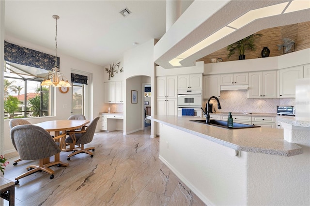 kitchen featuring white double oven, sink, pendant lighting, an inviting chandelier, and white cabinets