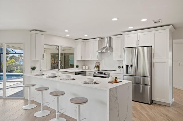 kitchen featuring sink, stainless steel appliances, white cabinetry, and wall chimney exhaust hood