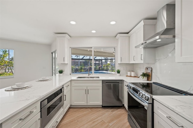 kitchen with light stone counters, white cabinets, wall chimney exhaust hood, and stainless steel appliances