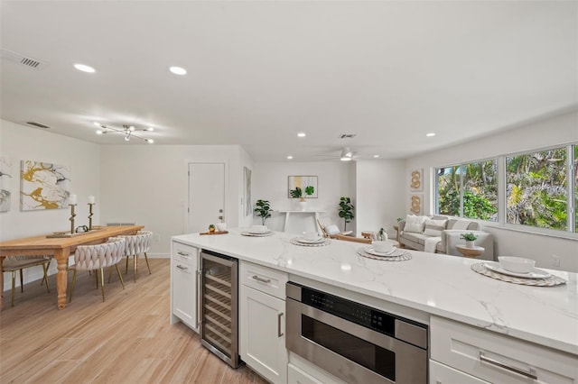 kitchen with light hardwood / wood-style floors, light stone countertops, white cabinets, and wine cooler