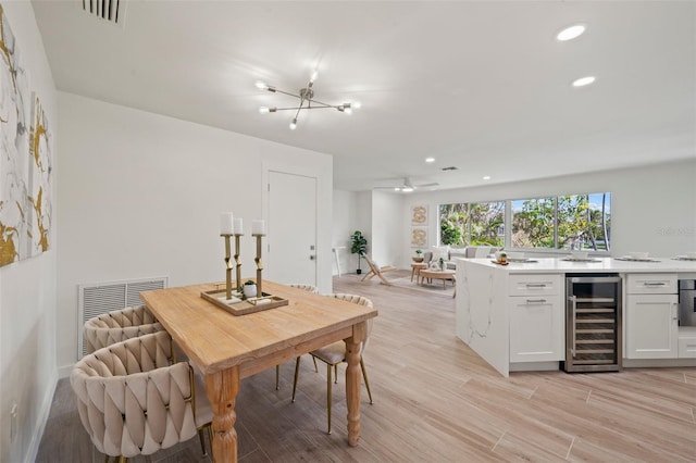 dining room with ceiling fan with notable chandelier, light wood-type flooring, and wine cooler